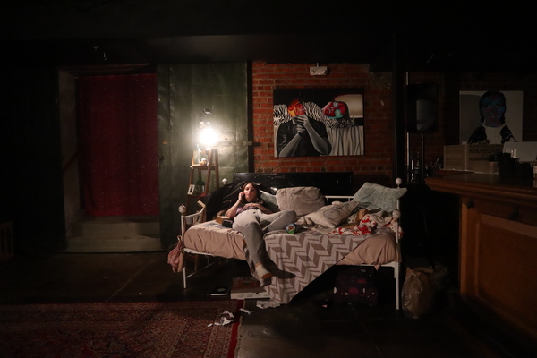 a character in sweats taking a phone call while splayed out across an untidy bed